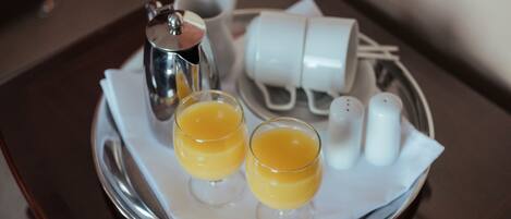 Una bandeja con dos vasos de jugo de naranja, una cafetera de plata y un juego de tazas y platones blancos.