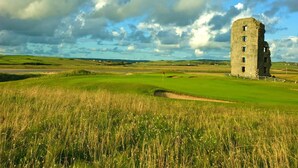 Una torre de piedra histórica en un campo cubierto de césped, con un campo de golf al fondo.