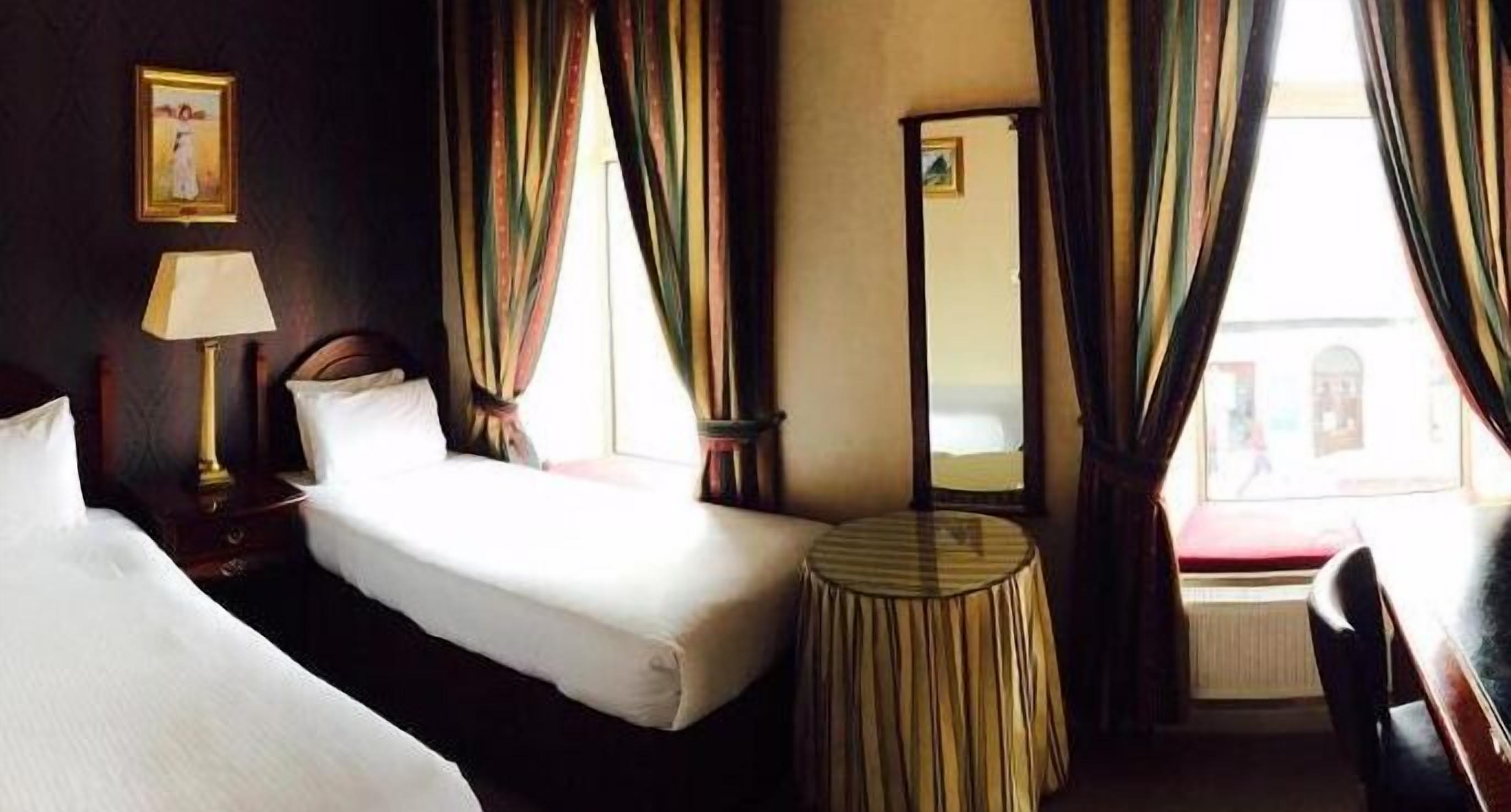Una habitación de hotel con dos camas, una mesa redonda, una lámpara y un espejo.