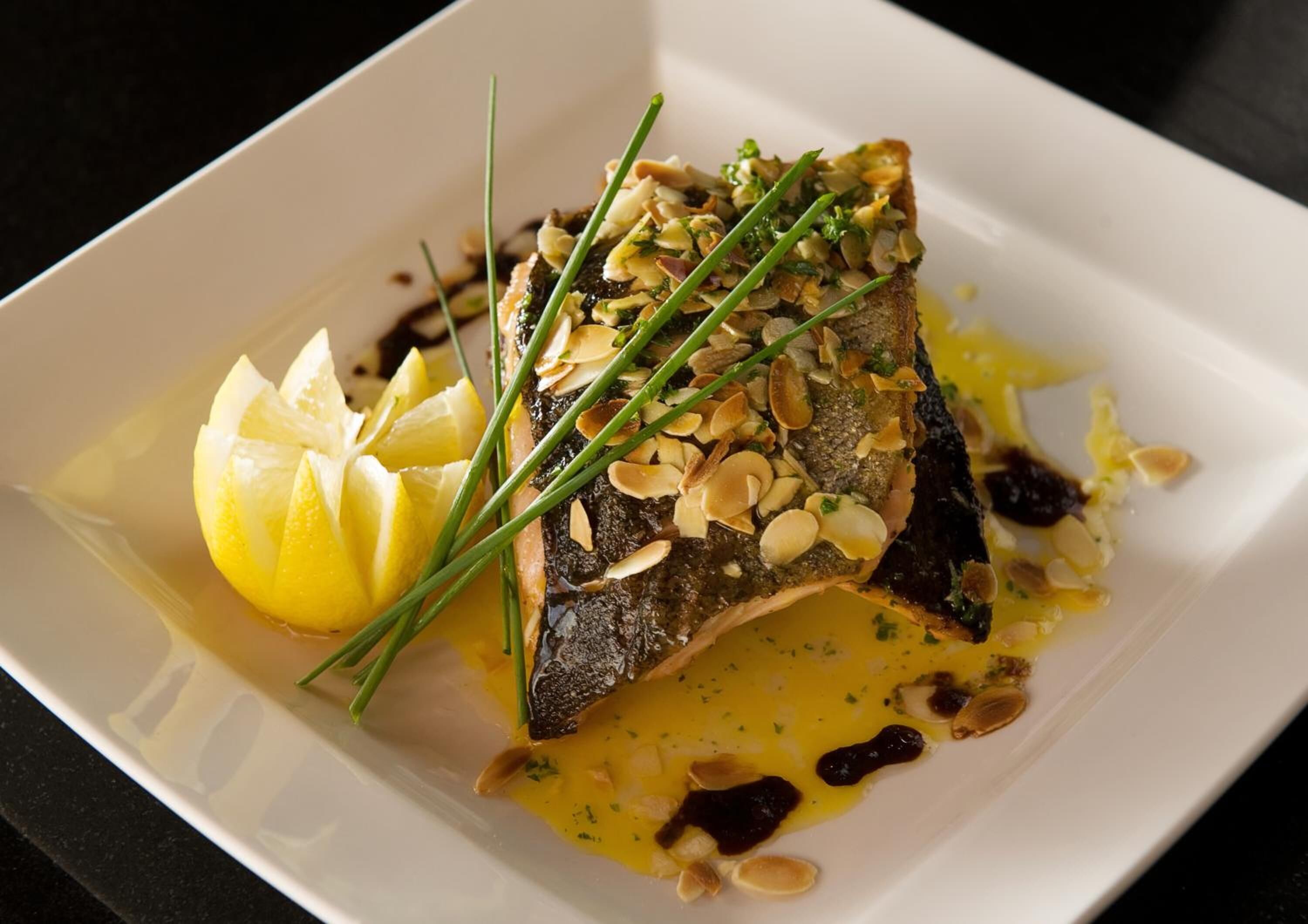 A dish with fish, lemon, and almonds on a white plate.