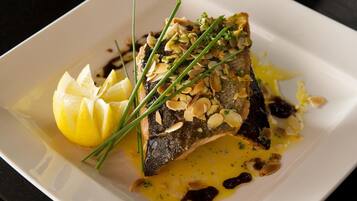 A dish with fish, lemon, and almonds on a white plate.