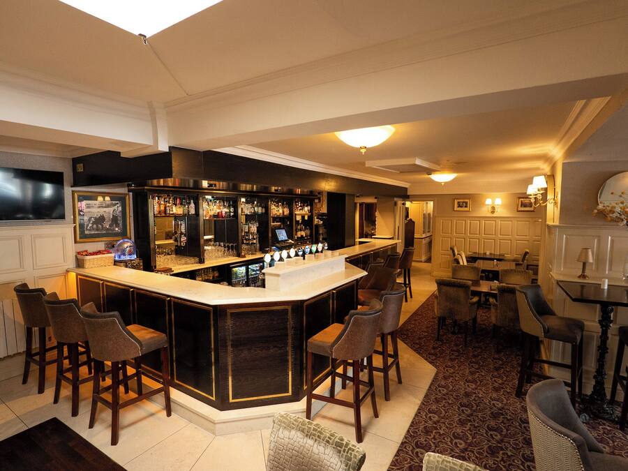 A bar area with a counter, multiple bar stools, and a television screen.