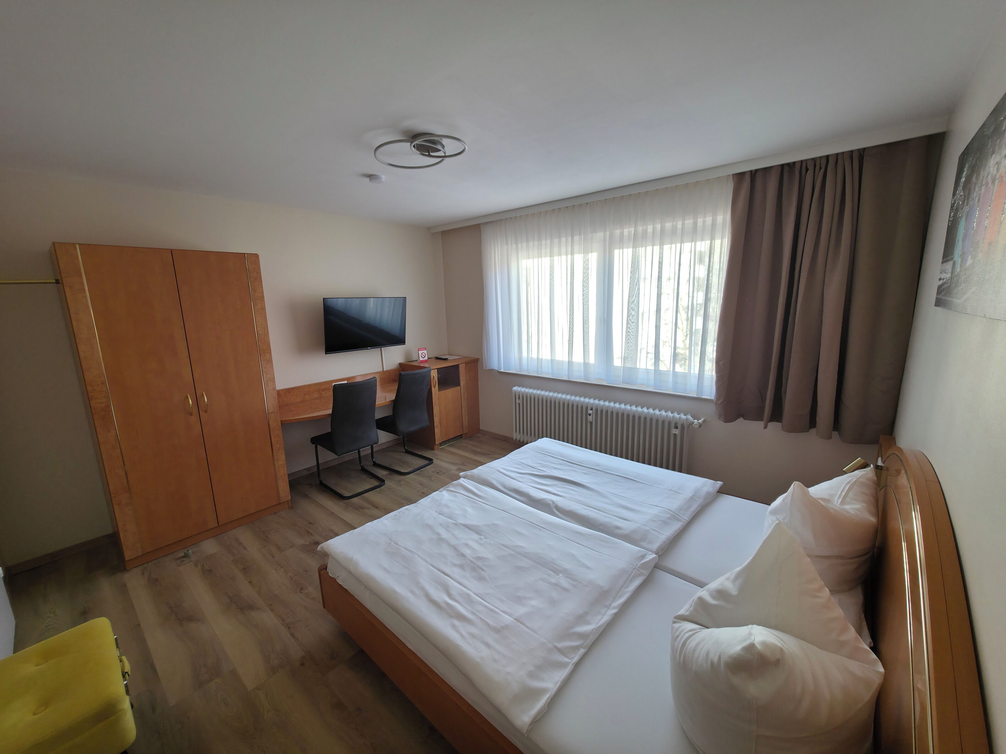 A hotel room with a bed, a desk with two chairs, a television, and a wardrobe.
