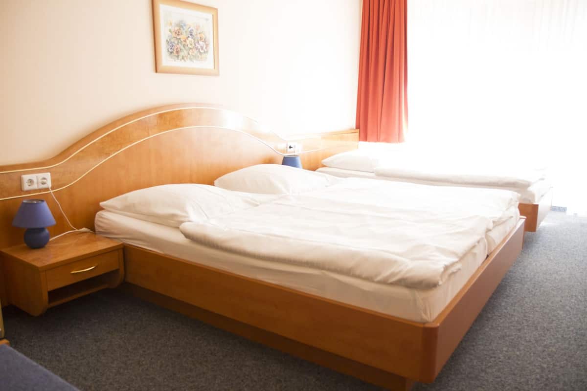 A hotel room with a wooden bed, two bedside tables, a lamp, and a painting on the wall.