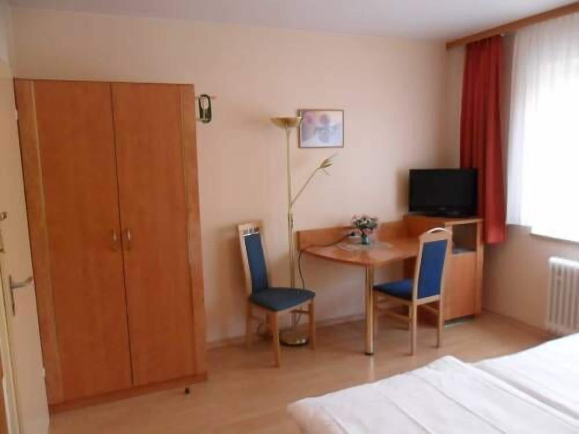 A hotel room with a bed, a desk with two chairs, a television, and a wardrobe.