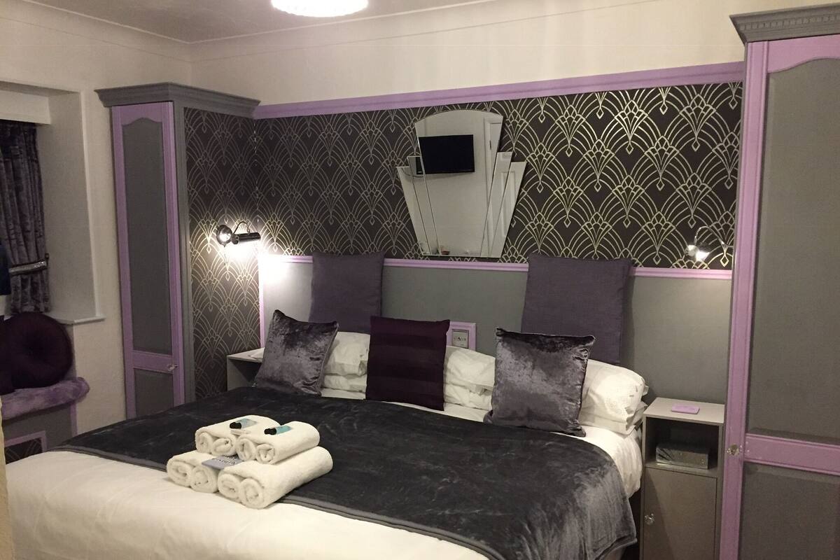 A neatly made bed with white and dark grey linens, a headboard with a decorative pattern, and a bedside table with a lamp.