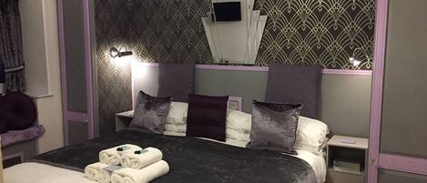 A neatly made bed with white and dark grey linens, a headboard with a decorative pattern, and a bedside table with a lamp.