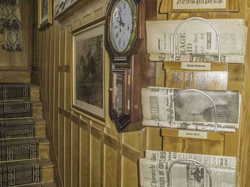Una pared con un reloj, un cuadro enmarcado y recortes de periódico.