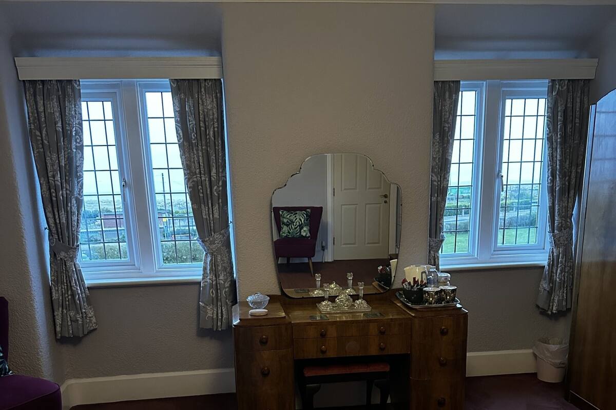 A hotel room with a large bed, a wooden dresser, a mirror, and two windows with curtains.