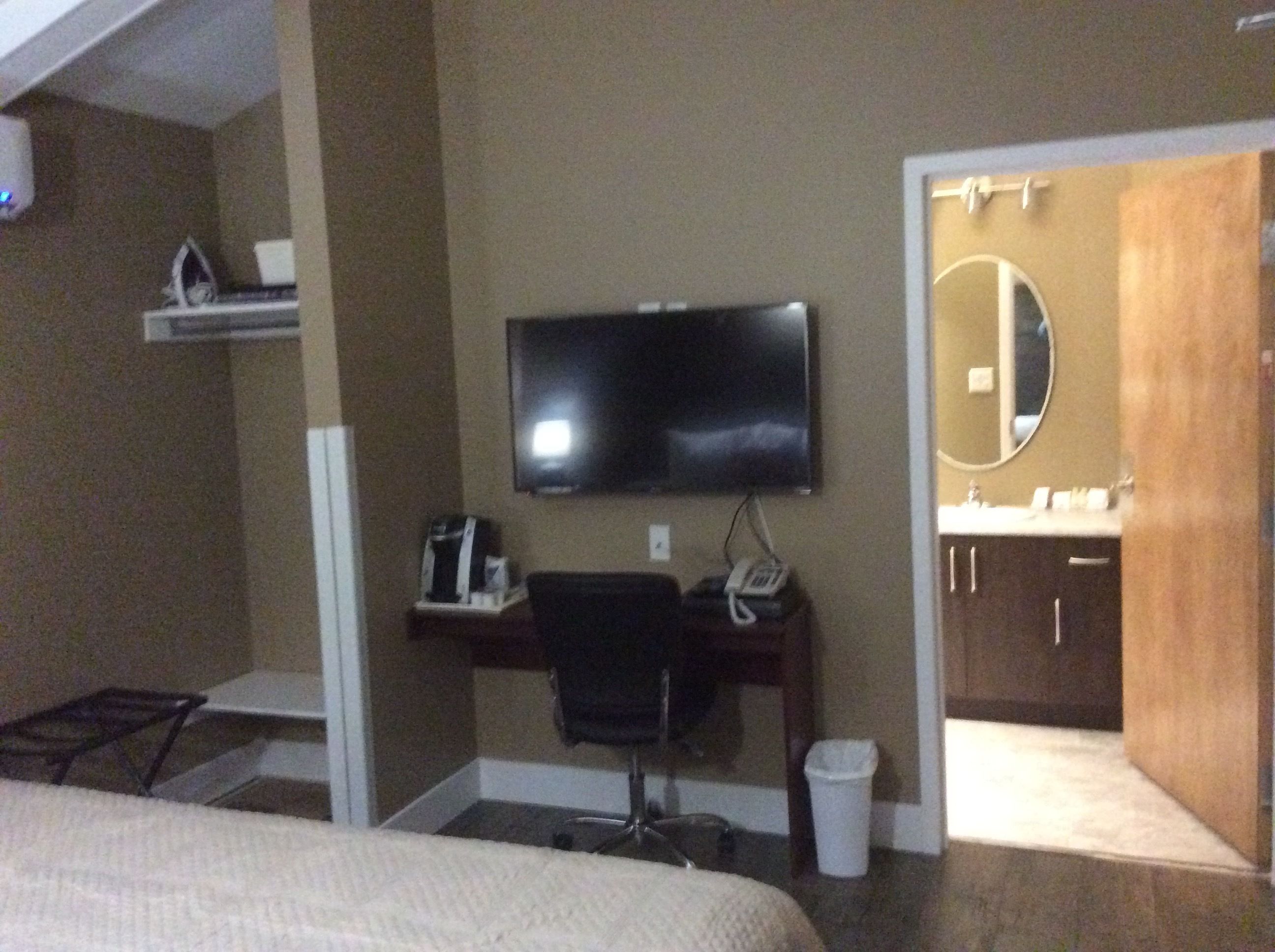 Camera d'albergo con un letto, una scrivania con una sedia, una televisione, un telefono e un bagno con uno specchio.