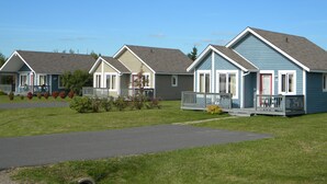 A row of single-story houses with front porches, a grassy lawn, and a clear sky.