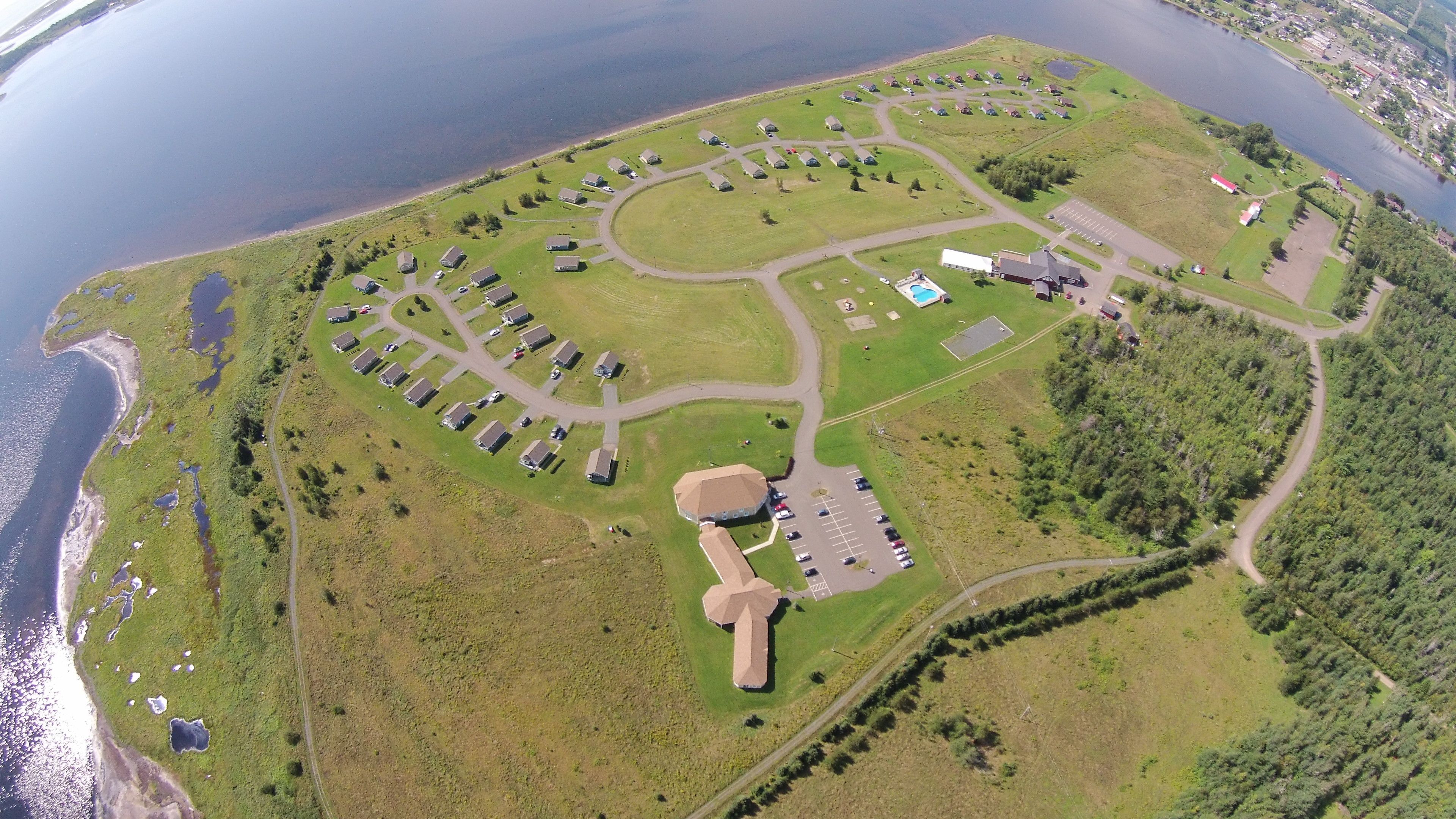 An aerial view of a campground with RV parking, a swimming pool, and a large building with a unique roof structure.