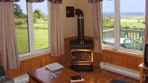 A cozy room with a wood-burning stove, large windows with curtains, a wooden table, and a view of the outdoors.