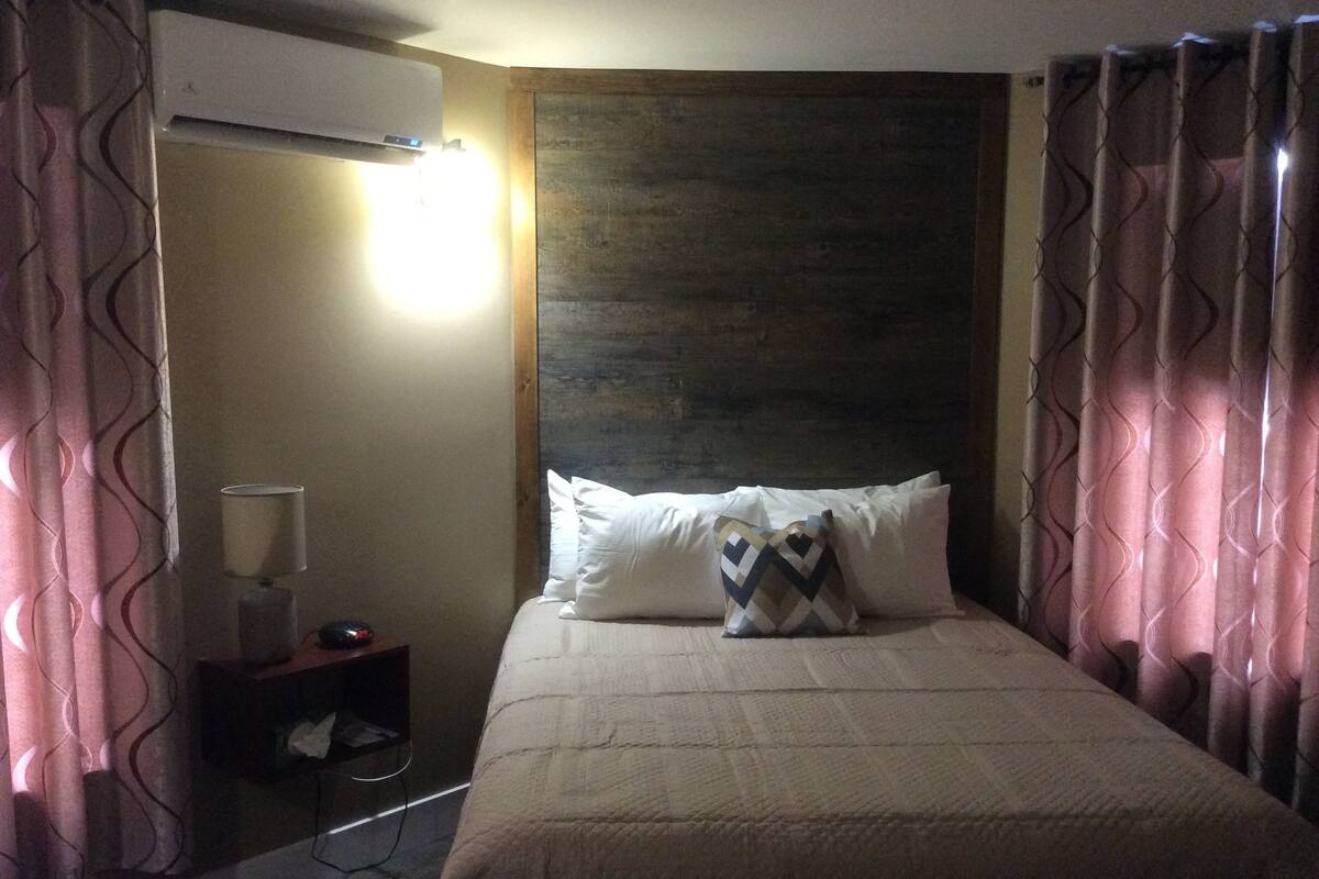 Een hotelkamer met een bed, nachtkastje, airconditioning en gordijnen.