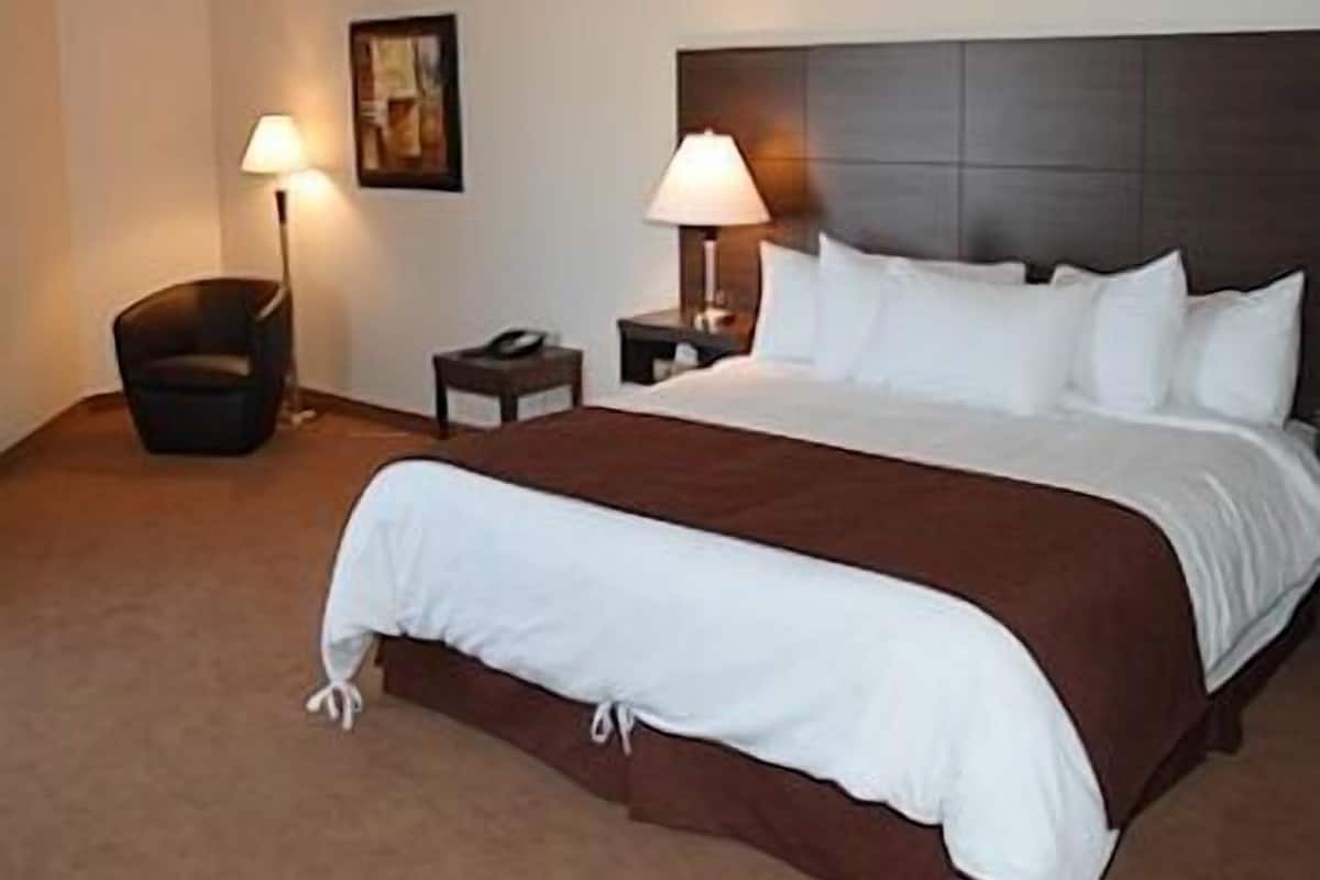 Een hotelkamer met een groot bed, twee nachtkastjes, een stoel en twee wandlampen.