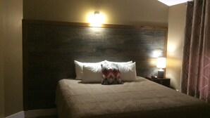 A hotel room with a large bed, a wooden headboard, a nightstand with a lamp, and a window with curtains.