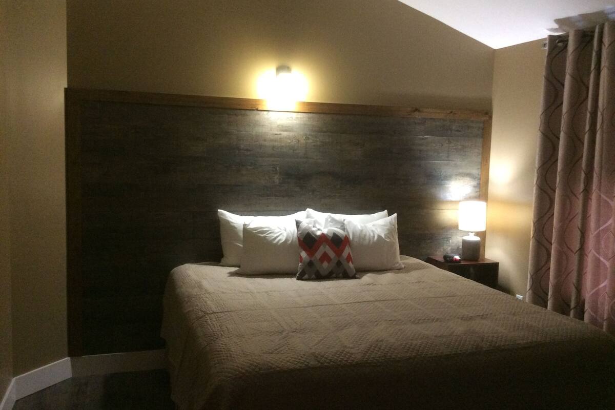 Een hotelkamer met een groot bed, een houten hoofdbord, een nachtkastje met een lamp en een raam met gordijnen.