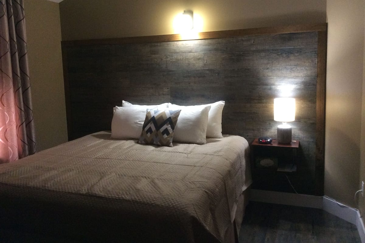Een net opgemaakt bed met een gekleurd kussen, een bedlampje en een houten hoofdbord.
