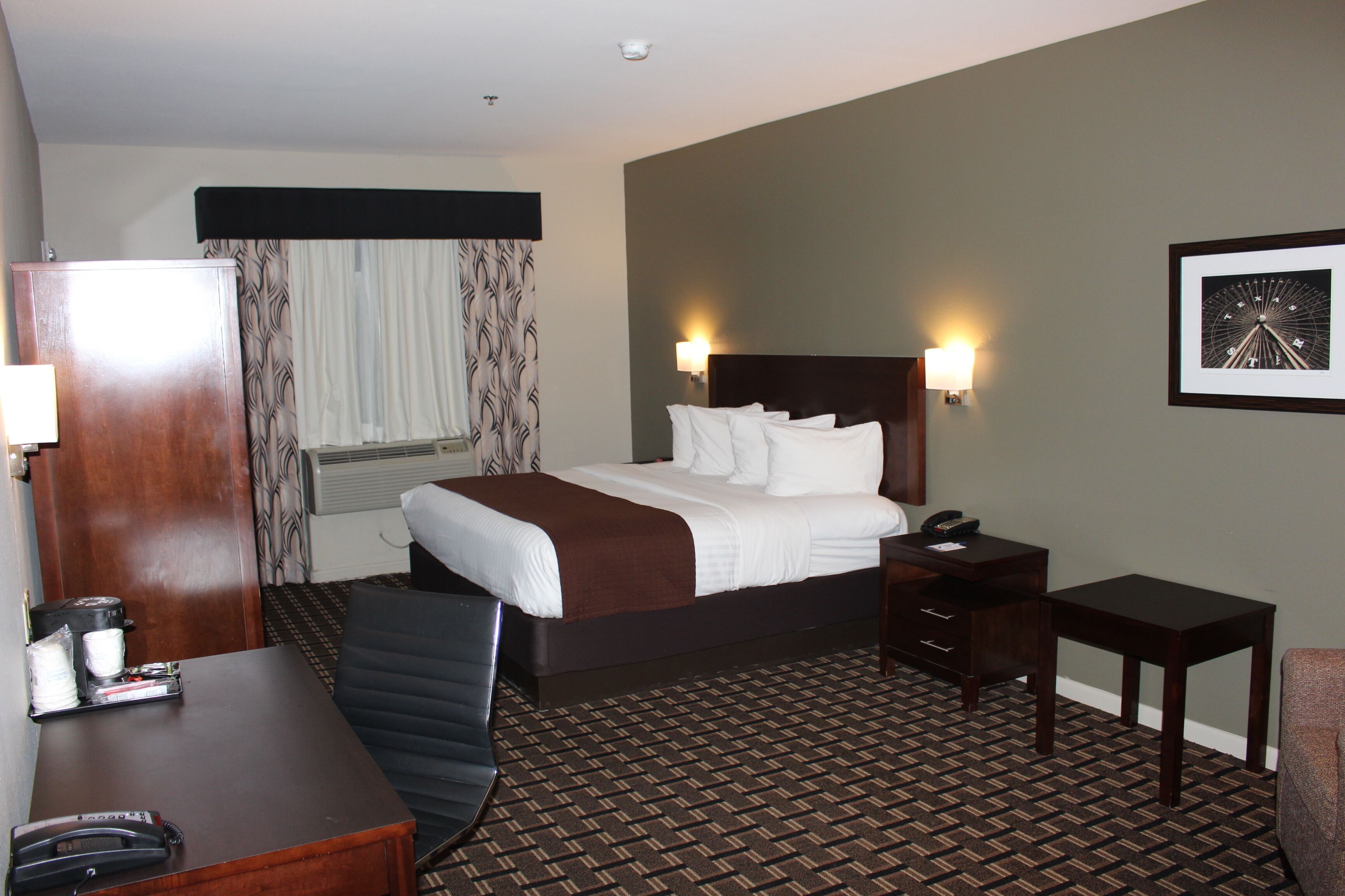 A hotel room with a bed, bedside tables, a desk, a chair, and a framed picture on the wall.