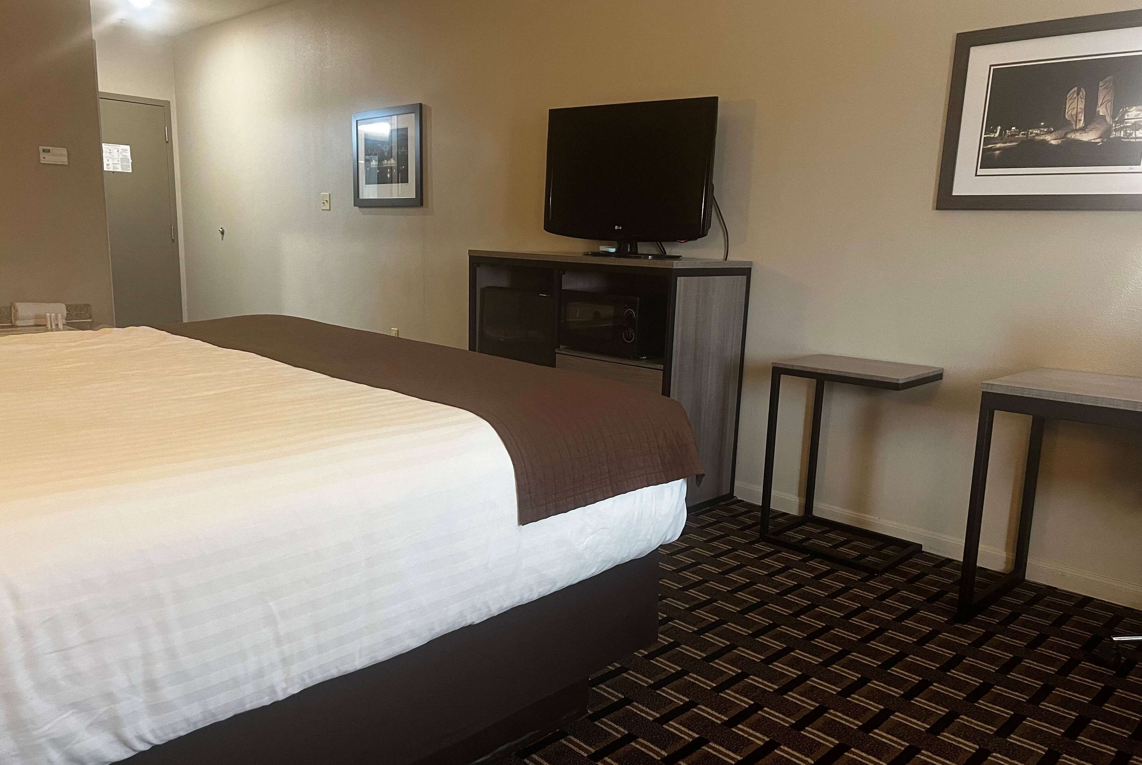 A hotel room with a large bed, a television on a stand, a small table, and a patterned carpet.