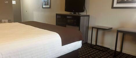 A hotel room with a large bed, a television on a stand, a small table, and a patterned carpet.