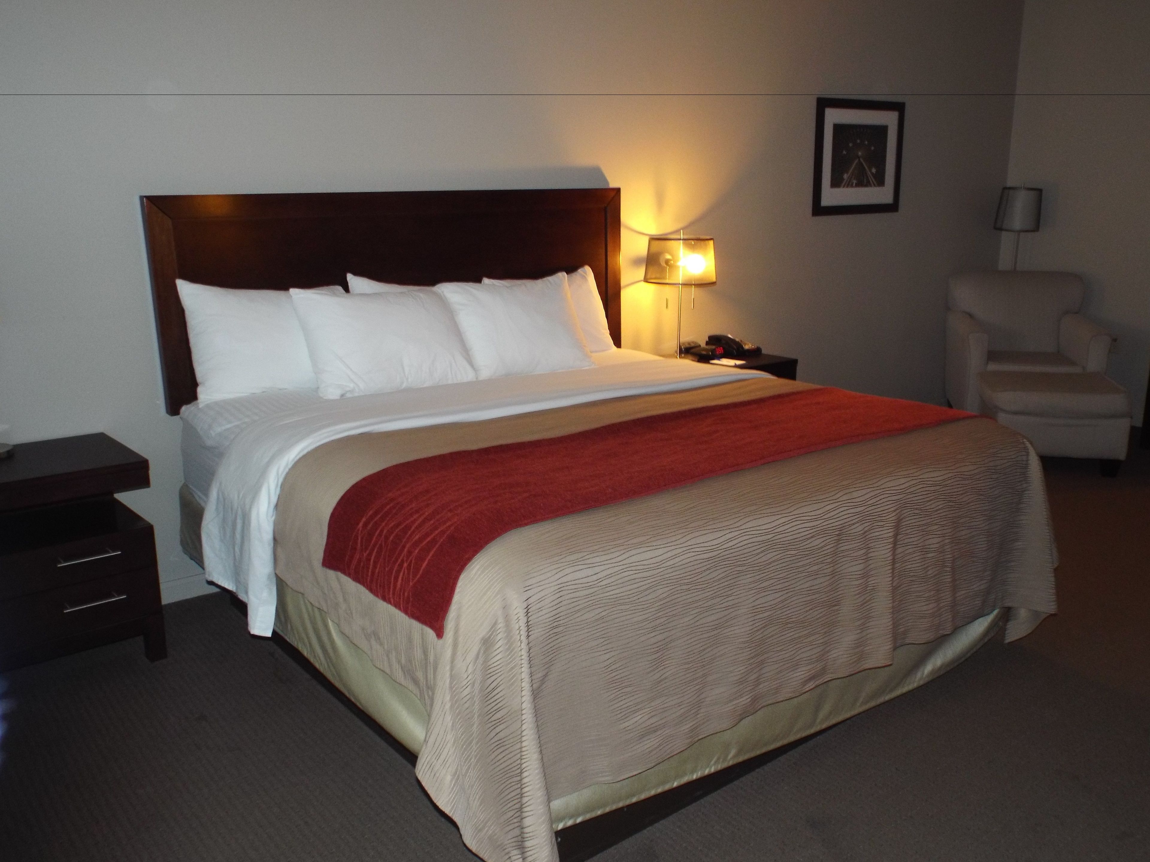 A hotel room with a large bed, a nightstand, a chair, and a wall-mounted lamp.