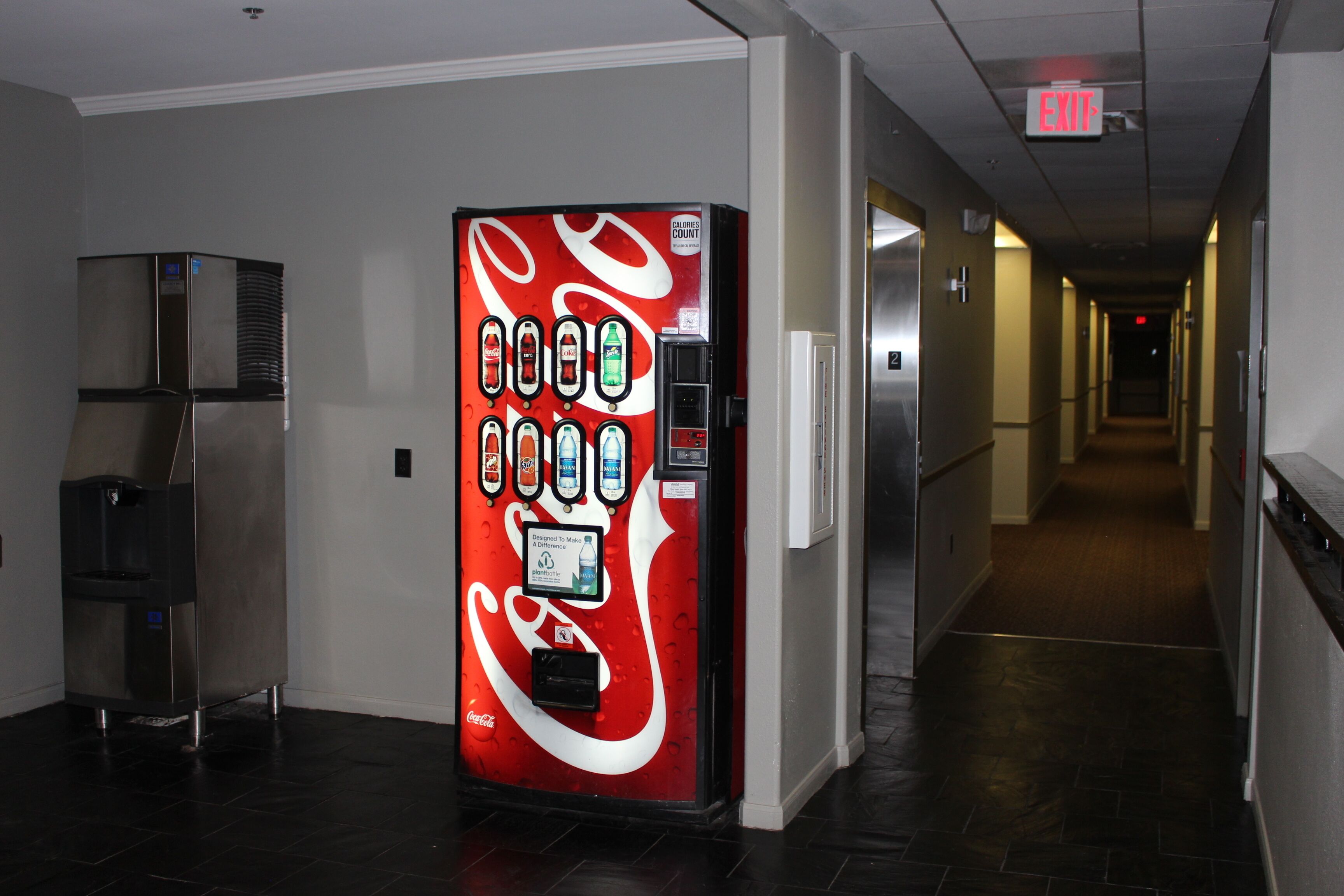 A hallway with a Coca-Cola vending machine and a refrigerator.