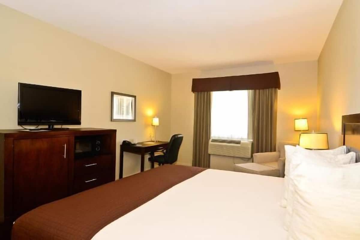 Ein Hotelzimmer mit einem Bett, einem Schreibtisch, einem Fernseher und einem Fenster mit Vorhängen.