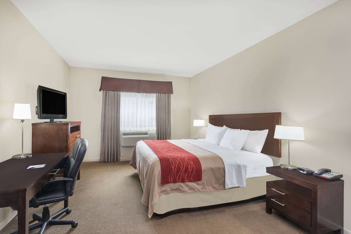 Ein Hotelzimmer mit Bett, Schreibtisch, Stuhl, Fernseher und einem Fenster mit Vorhängen.