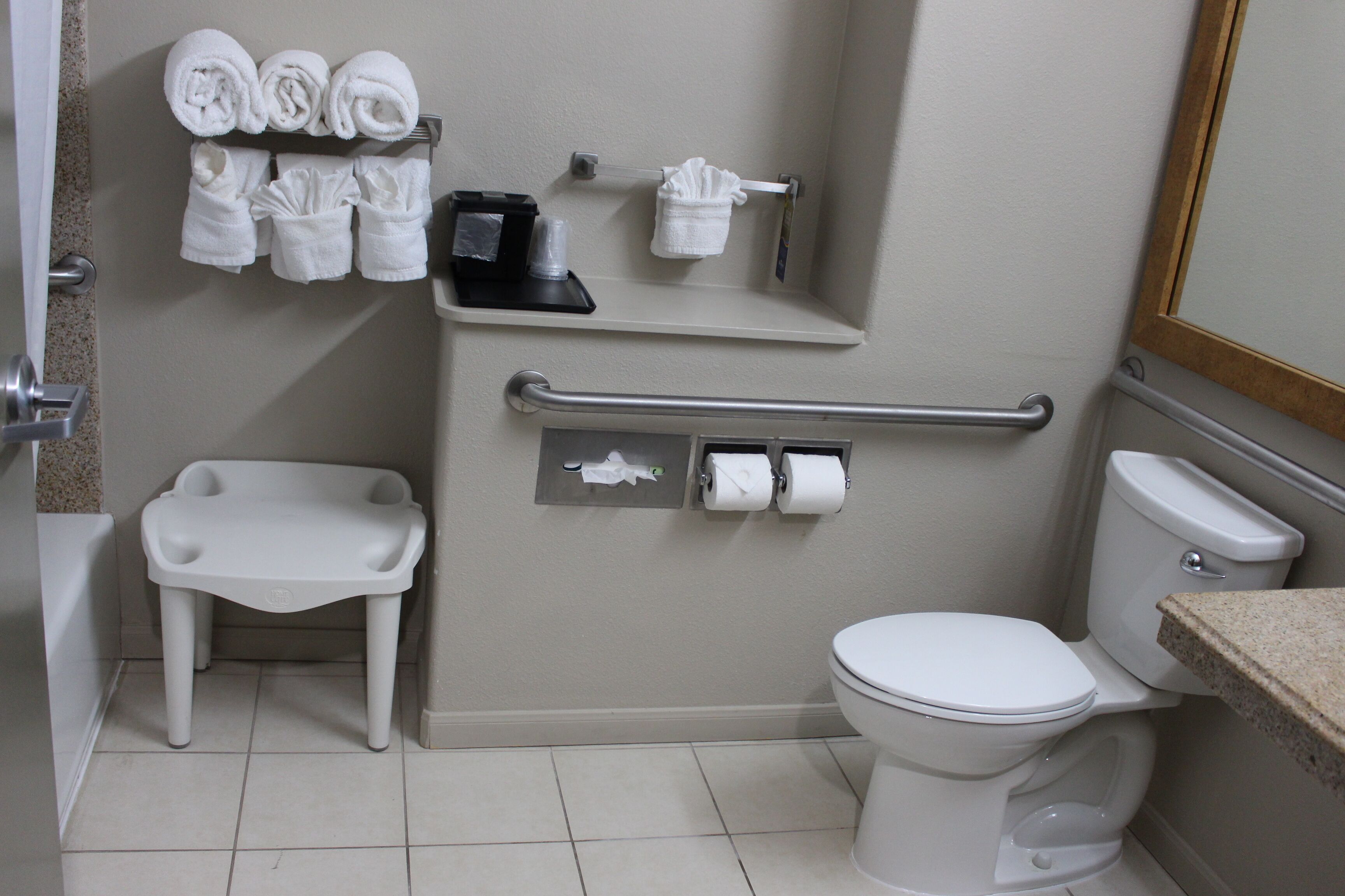 Un baño con inodoro, lavamanos, toallero con toallas, secamanos y dispensador de papel higiénico.
