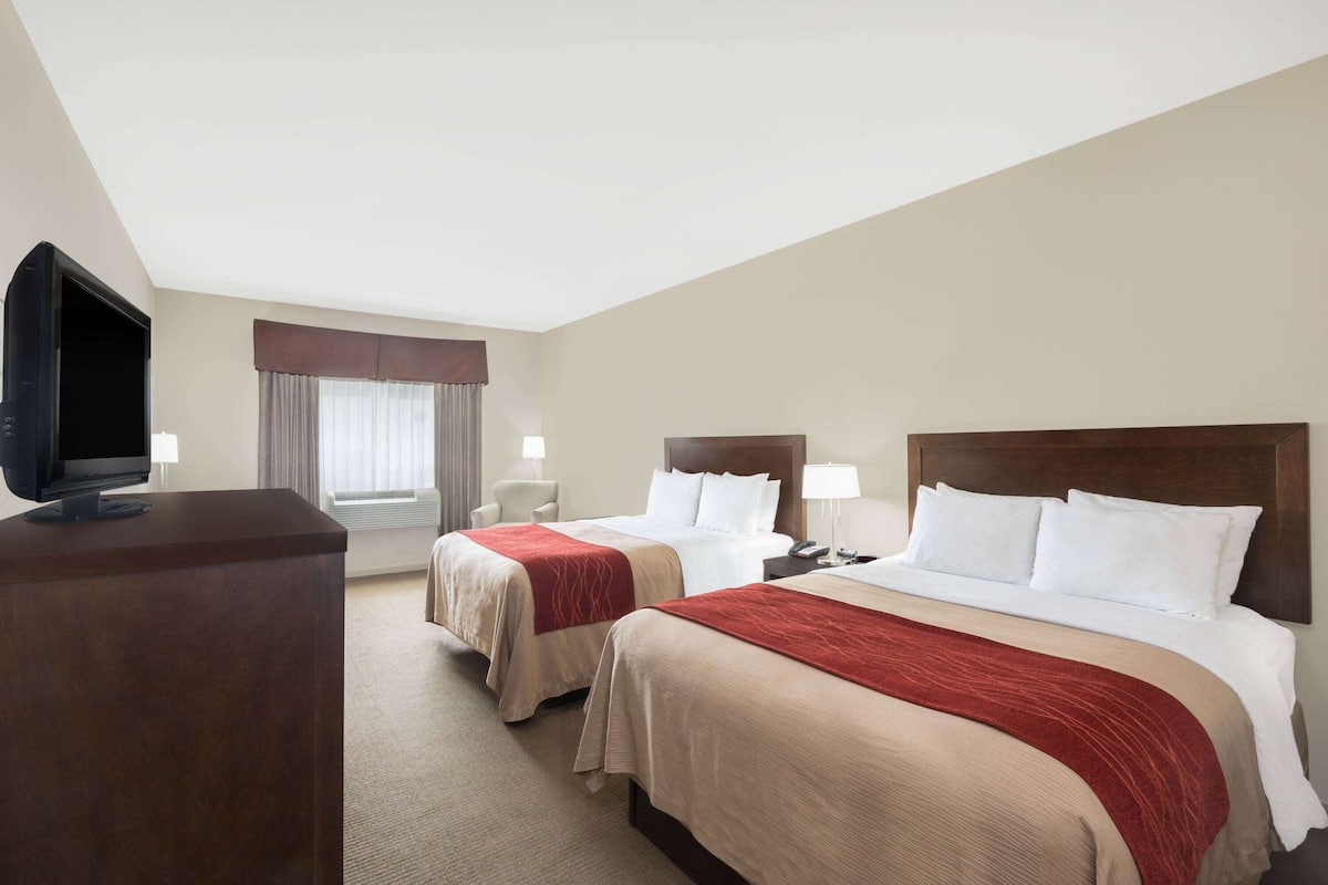 Ein Hotelzimmer mit zwei Betten, einem Fernseher, einem Schreibtisch und einem Fenster mit Vorhängen.