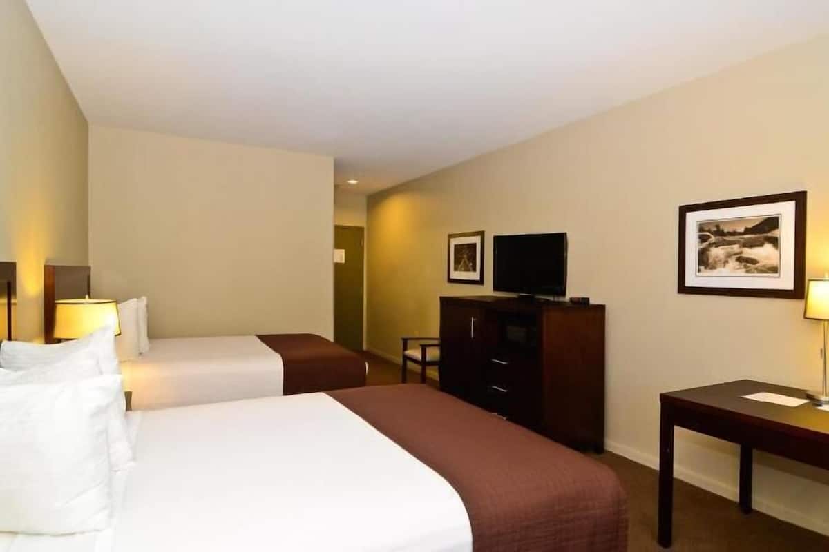 Ein Hotelzimmer mit zwei Betten, einem Fernseher, einem Schreibtisch und einem Stuhl.