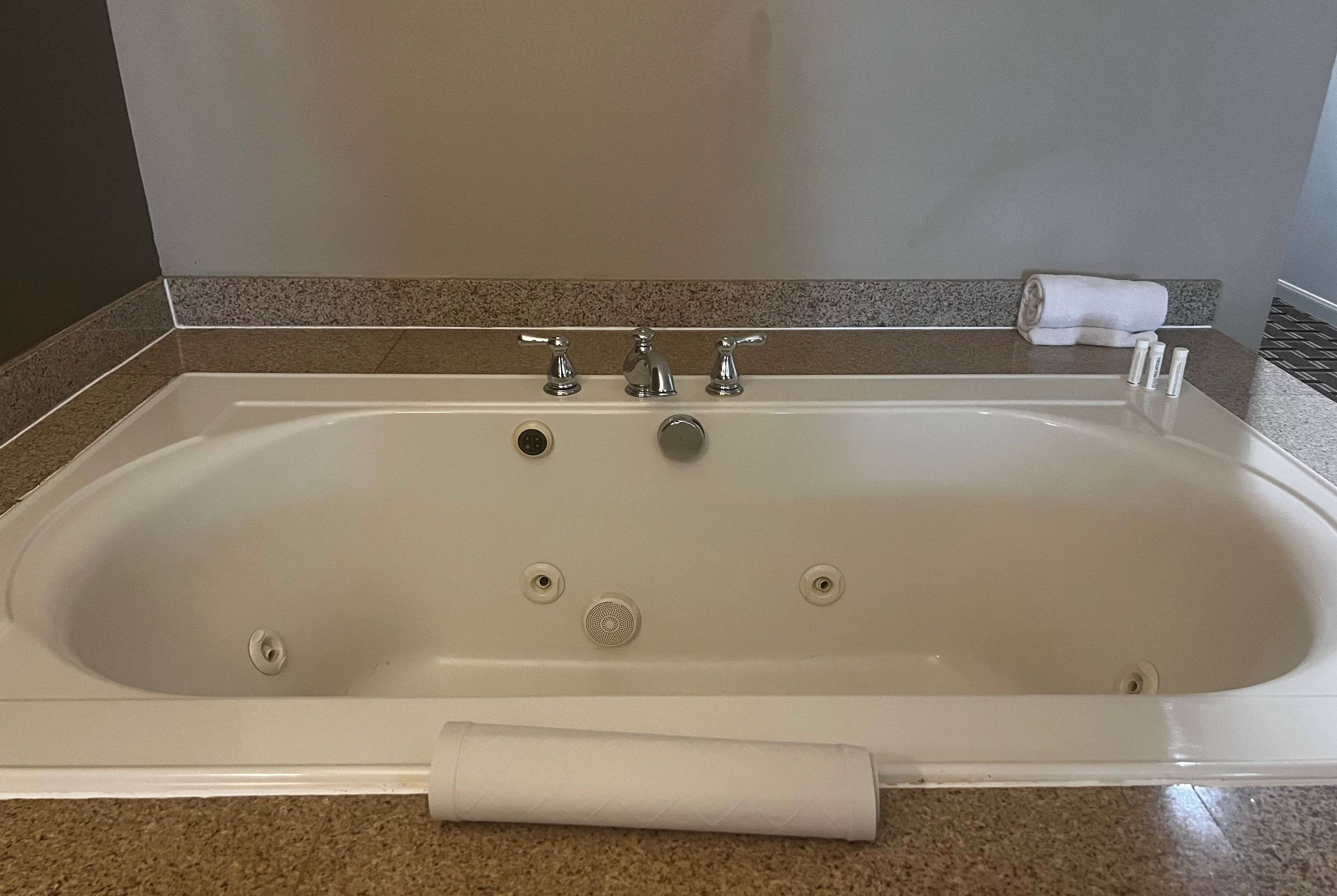 A rectangular bathtub with three faucets, a handheld showerhead, and a towel on the side.