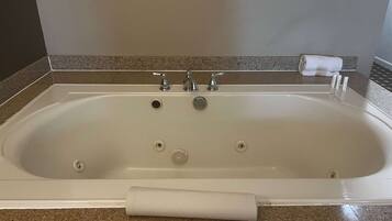 A rectangular bathtub with three faucets, a handheld showerhead, and a towel on the side.