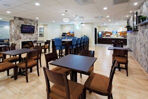 A restaurant with multiple tables and chairs, a television mounted on the wall, and a counter with a coffee machine. - Holiday Inn Express Benicia by IHG (Benicia)