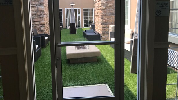 A view through a glass door into a courtyard with artificial grass, outdoor furniture, and a stone wall. - Holiday Inn Express Benicia by IHG (Benicia)