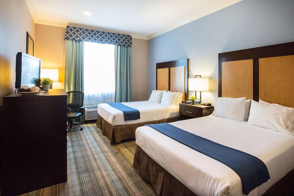 A hotel room with two beds, a desk, a chair, a television, and a window with curtains.