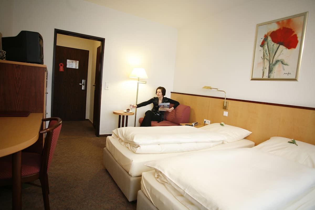 Ein Hotelzimmer mit zwei Betten, einem Schreibtisch, einem Stuhl, einer Lampe und einer Tür.