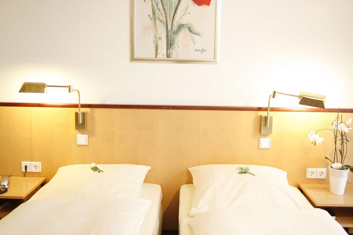 Ein Hotelzimmer mit zwei Einzelbetten, einem Holzkopfteil, Nachttischlampen, einem Bilderrahmen mit einer Blumenmalerei und einer Orchidee im Blumentopf auf dem Nachttisch.