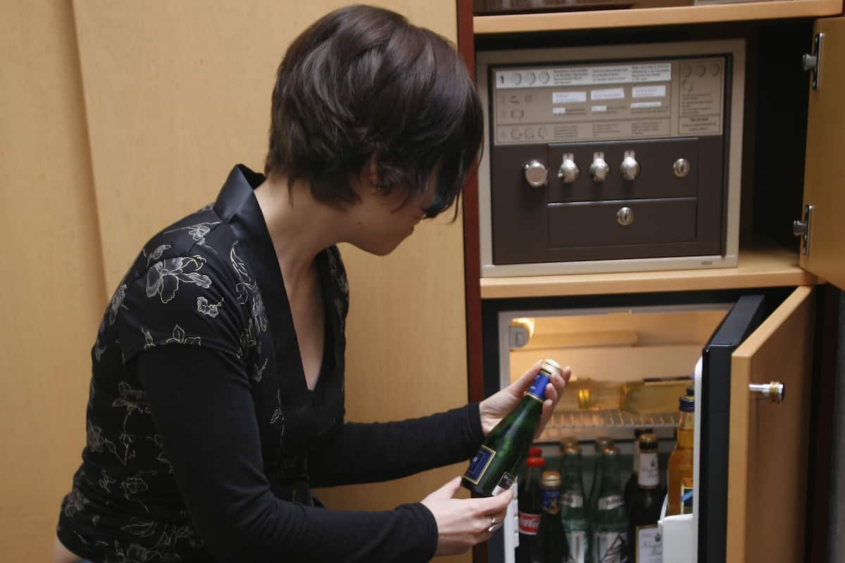Eine Person öffnet eine Minibar in einem Zimmer mit einem Holzkabinett darüber.