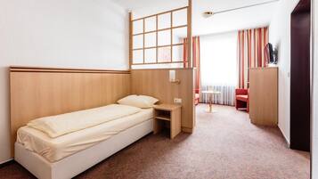 Una habitación de hotel con una cama individual, una mesita pequeña, un escritorio y un armario.