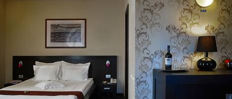 A hotel room with a neatly made bed, a bedside table with a phone and a bottle, and a wall-mounted light fixture.