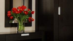 Un armario de madera oscura con un espejo encima y una mesita con un florero de flores rojas.