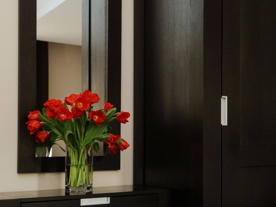 A dark wooden wardrobe with a mirror above it and a small table with a vase of red flowers.