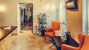 Zona de recepción con mostrador, una planta en maceta y dos sillones naranjas.