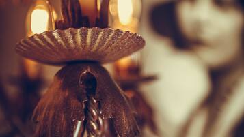 A close-up of a candle holder with a lit candle, a spiral design, and a blurred background with a framed picture.