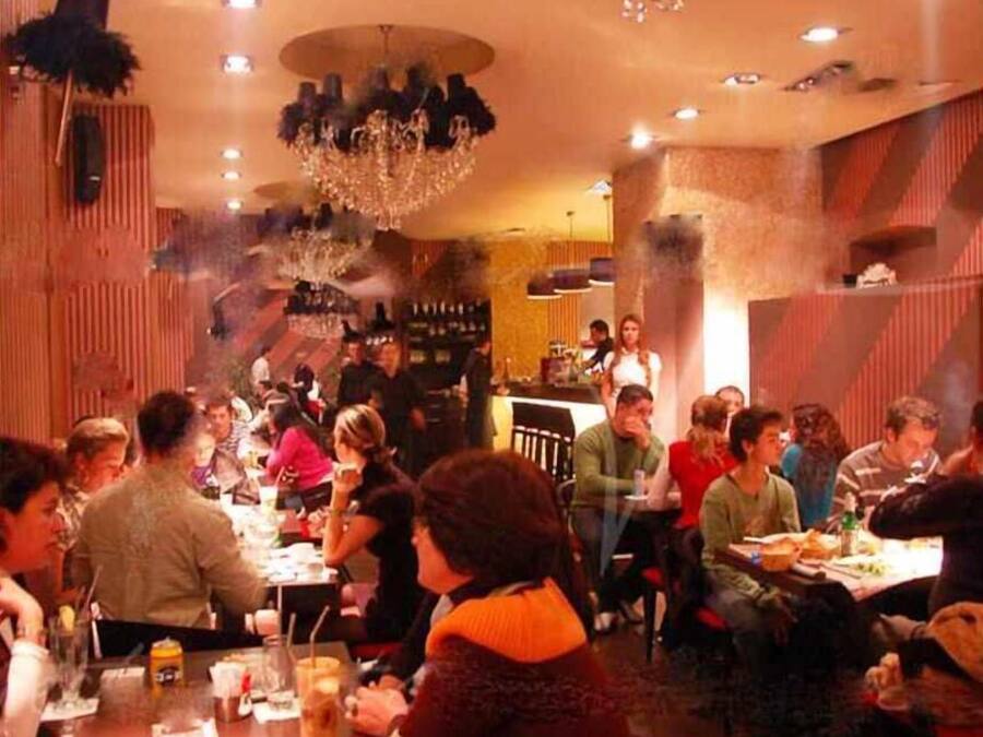 Um restaurante movimentado com mesas, cadeiras, um bar e um lustre.