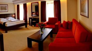 A hotel room with a bed, a red sofa, a coffee table with flowers, and a desk with a lamp.