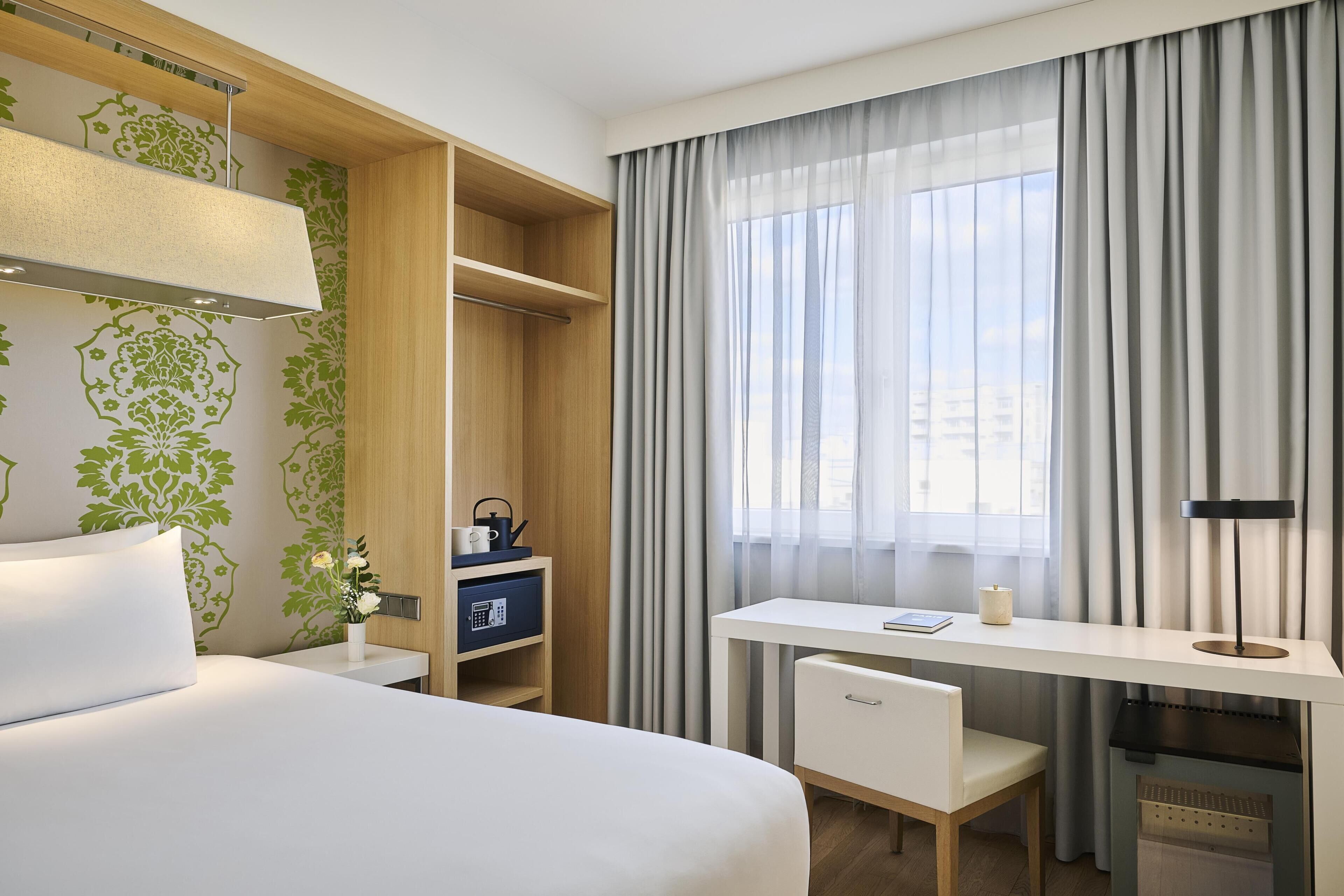 Habitación de hotel con cama, escritorio, silla, armario y ventana con cortinas.