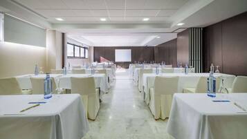 Une salle de conférence avec des rangées de tables, chacune étant équipée d’une bouteille d’eau, d’un verre et d’un bloc-notes.